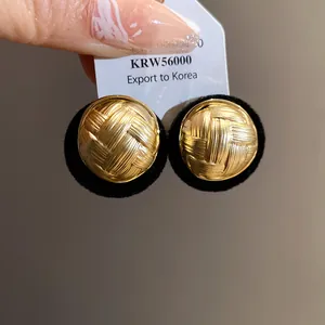 Close-up macro detail of gold round stud earrings with an intricate woven pleated texture