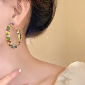 Detailed view of a woman wearing large gold hoop earrings decorated with colorful crystal beads