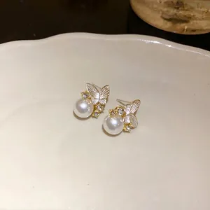 Eleganti orecchini a perno a farfalla con perle e strass su un piatto in ceramica bianca