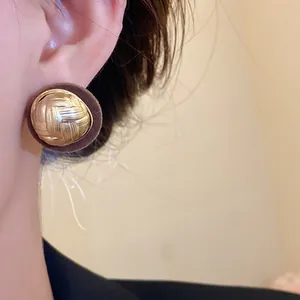 Close-up of vintage round stud earring with gold woven texture and brown flocked border