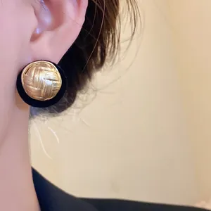 Close-up view of retro round gold woven stud earrings with black flocked border deco