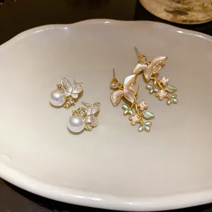 Dettaglio di eleganti orecchini a farfalla e ramo floreale in argento su un piatto di ceramica.