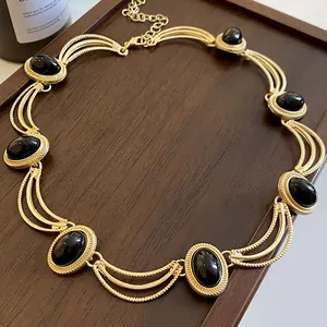 Gros plan d'un collier vintage doré avec pierres ovales noires sur plateau en bois.