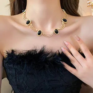 Collier de style palais vintage avec des maillons dorés ovales et des perles noires sur modèle.