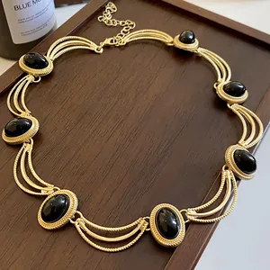Gros plan d'un collier de style cour rétro avec des pierres ovales noires sur plateau bois.