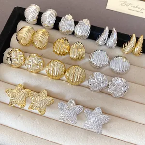 Close-up of gold and silver acrylic stud earrings with pleated and ribbed textures.