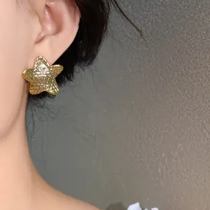 Close-up view of a minimalist gold star earring with quilted texture worn on ear