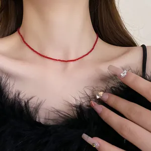 Close-up of a minimalist red beaded choker necklace worn with a stylish black feather top.
