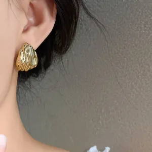 Detailed macro view of high-end golden rippled waterdrop stud earrings worn on female ear