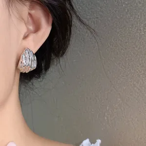 Close-up of silver pleated teardrop stud earring worn on ear, showing metallic texture.