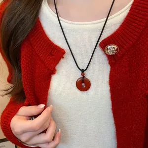 Close-up of a red agate donut pendant necklace worn over a white shirt and red cardigan.
