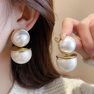 Elegant double pearl drop earrings with gold disc accent shown on ear and hand.