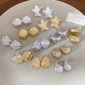 Detailed view of various gold and silver metallic earrings with pleated textures on a plate