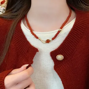 Detailed close-up view of a red agate bead necklace with a golden pendant on a model