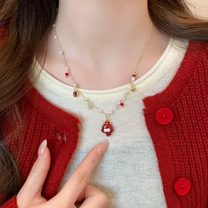 Close-up of a gold necklace with red pendant and pearls on a model wearing a red cardigan