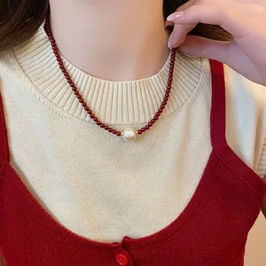 Detailed close-up of a red agate beaded necklace with a central pearl on a model.