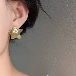 Detailed close-up of a minimalist textured gold star stud earring on a model's ear