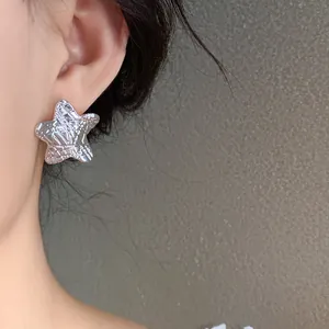 Close-up of a star-shaped silver quilted stud earring worn on a female model's ear.