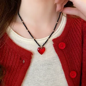 Detailed close-up showing an elegant red heart pendant necklace with black beaded chain on model