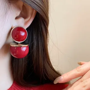 Close-up of red circular stud earrings with gold metal frame worn by a model