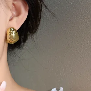 Close-up of golden pleated waterdrop stud earring showing intricate texture on the ear.