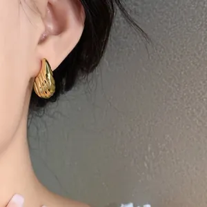 Close-up detail of golden pleated waterdrop stud earrings on model