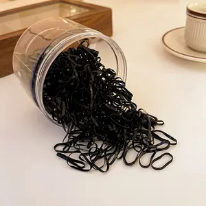 Close-up of disposable black elastic hair bands spilling from a clear container on a table