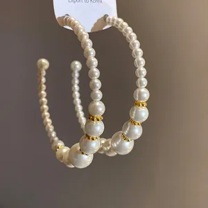Primo piano di eleganti orecchini a cerchio a C con perle bianche sfumate e distanziatori oro