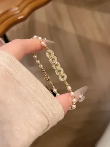Elegant gold-toned pearl bracelet with sparkling zirconia coin motifs shown on a hand