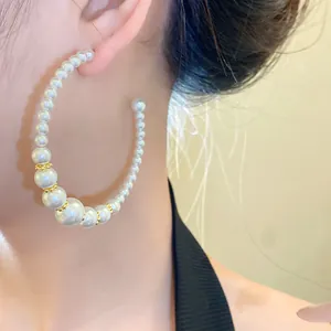 Primo piano di orecchino a cerchio a forma di C con perle bianche graduate sulla modella