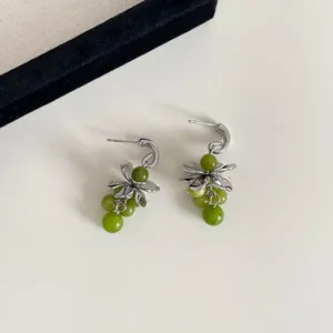 Detailweergave van groene glazen druiventas oorringen met zilveren bloemendetails