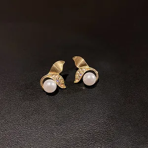 Dettaglio di orecchini a coda di pesce vintage in oro con perle bianche e cristalli