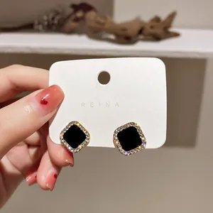 Primo piano di eleganti orecchini a perno neri quadrati con bordo in strass su cartoncino