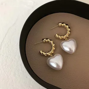 Dettaglio di orecchini a cerchio intrecciati dorati con eleganti pendenti a cuore.