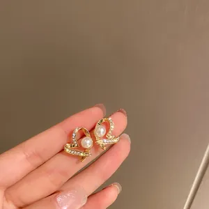 Primo piano di eleganti orecchini a cuore in oro con perla e strass brillanti in mano