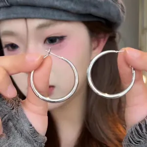 Large polished silver oval hoop earrings held by a model featuring a minimalist design