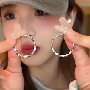 Minimalist silver hoop earrings featuring a textured cross design shown by a model