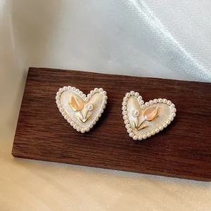 Primo piano di orecchini di perle a forma di cuore con dettaglio tulipano su legno