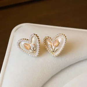 Dettaglio di orecchini a lobo a cuore con perle ed elegante motivo a tulipano oro