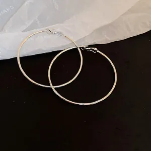 Elegant minimalist silver metallic hoop earrings displayed on a dark contrast surface