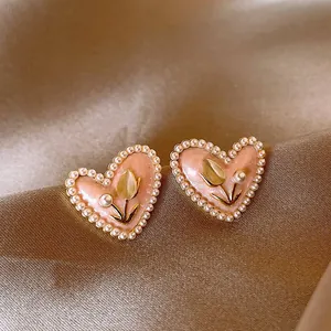 Dettaglio di eleganti orecchini a forma di cuore rosa con bordi di perle e tulipani