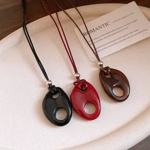 Gros plan de trois pendentifs ovales évidés en résine noir, rouge et marron brillant