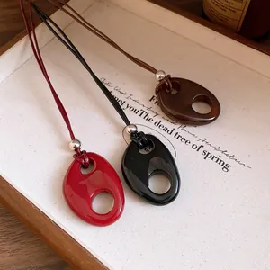 Détail macro de trois pendentifs ovales vintage en résine rouge, noire et marron.