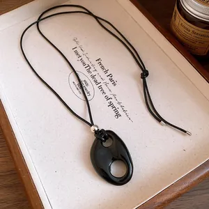 Détail d'un collier pendentif ovale creux en résine noire sur un plateau en bois