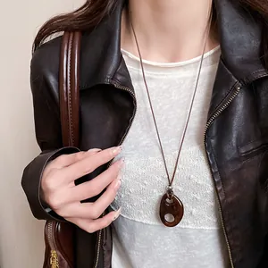 Gros plan d'un collier pendentif ovale creux en résine vintage sur cordon brun