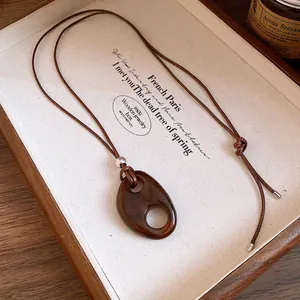 Détail du collier avec pendentif ovale en résine marron sur un plateau en bois