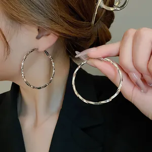 Detailed view of elegant large twisted silver hoop earrings shown on ear and held by hand