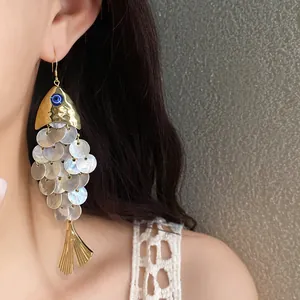 Primo piano di orecchini a forma di pesce d'oro con scaglie di conchiglia su una modella.