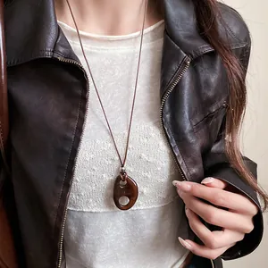Gros plan d'un collier vintage avec pendentif ovale en résine sur veste en cuir brun.