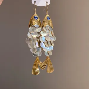 Dettaglio di orecchini a pesce dorati con scaglie di conchiglia e occhio della fortuna